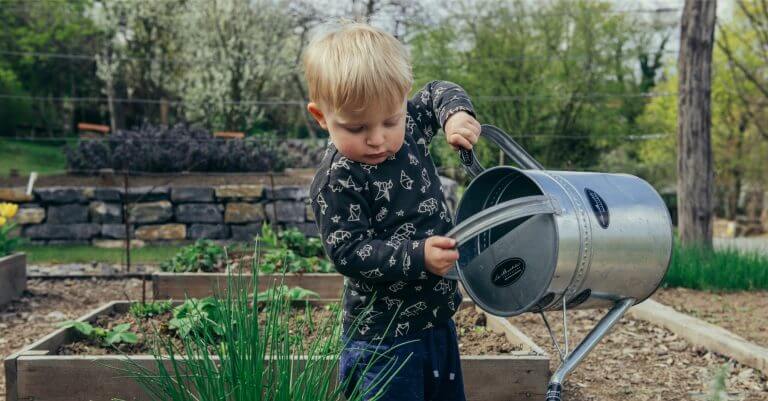 Junge im Garten gießt Pflanzen im Beet.