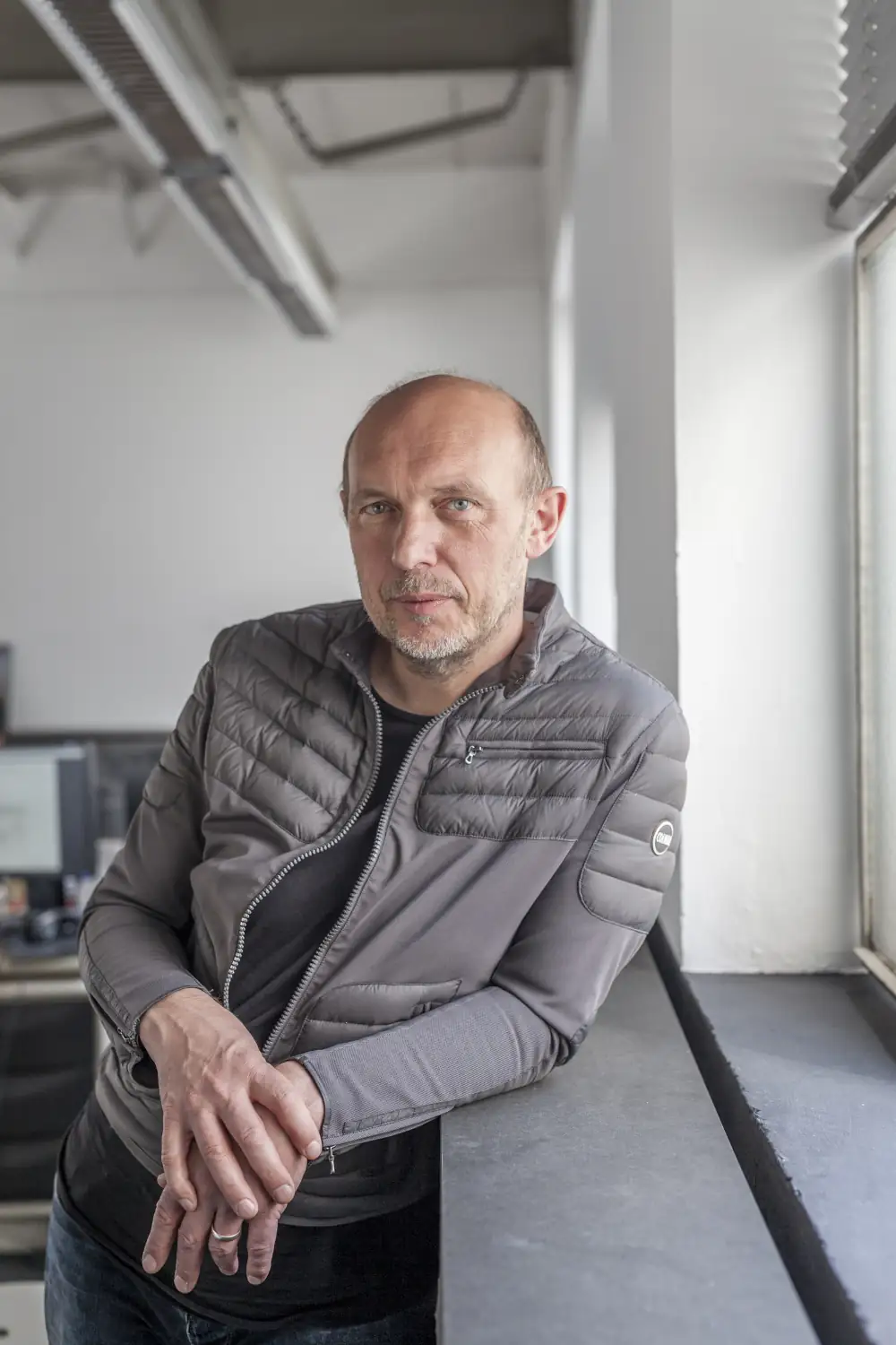 Porträtfoto von Architekt Peter Haimerl. Er lehnt sich mit dem linken Arm auf eine Fensterbank.