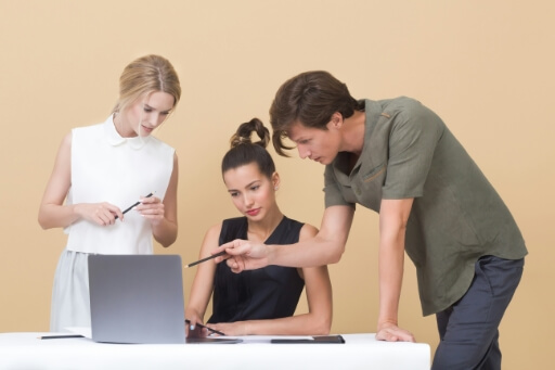 Zwei junge Frauen und ein Mann sitzen vor dem Laptop und untersuchen etwas. Analyse spielt eine große Rolle auf dem Immobilienmarkt Hamburg. 