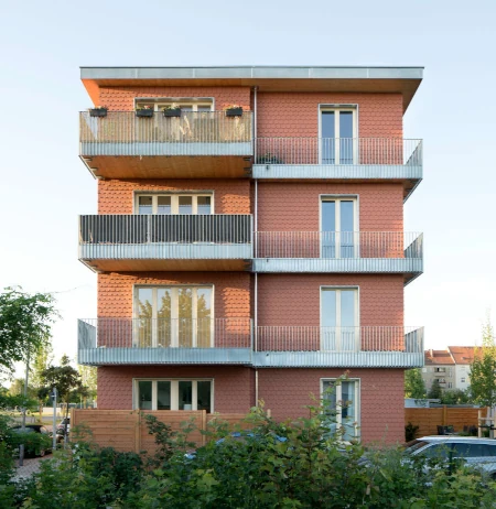 Massivholzhaus in Neuruppin. Es verfügt über eine rote Fassade mit tiefen Fenstern und einem Flachdach.