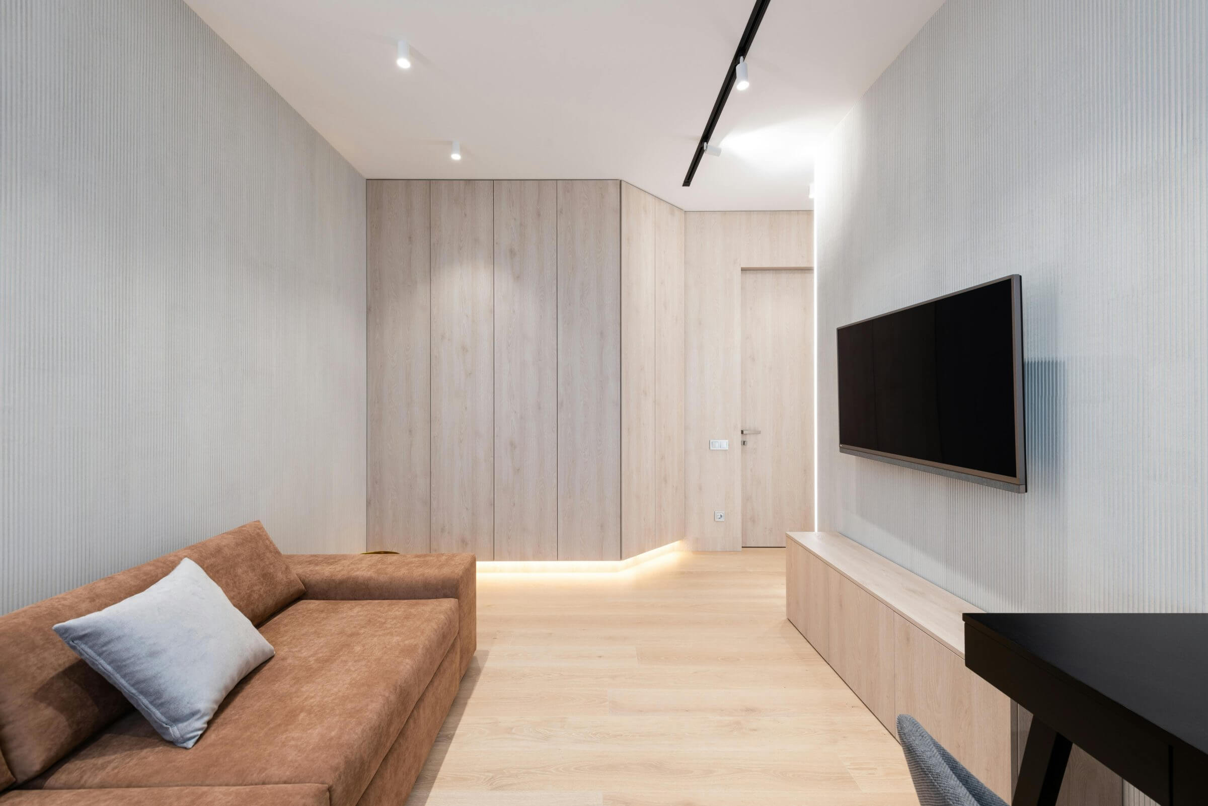 Minimalistisch eingerichtetes Wohnzimmer mit einer braunen Couch, einem Fernseher an der Wand und eleganter Holzverkleidung.