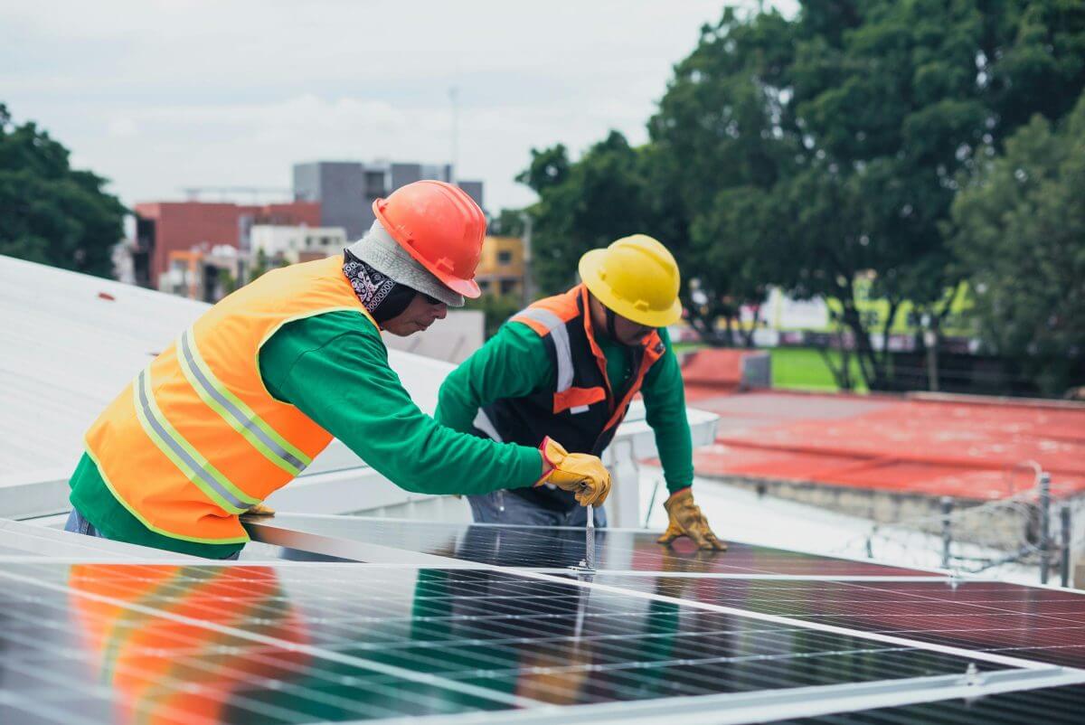 Zwei Bauarbeiter bringen Solarmodule auf einem Dach an.