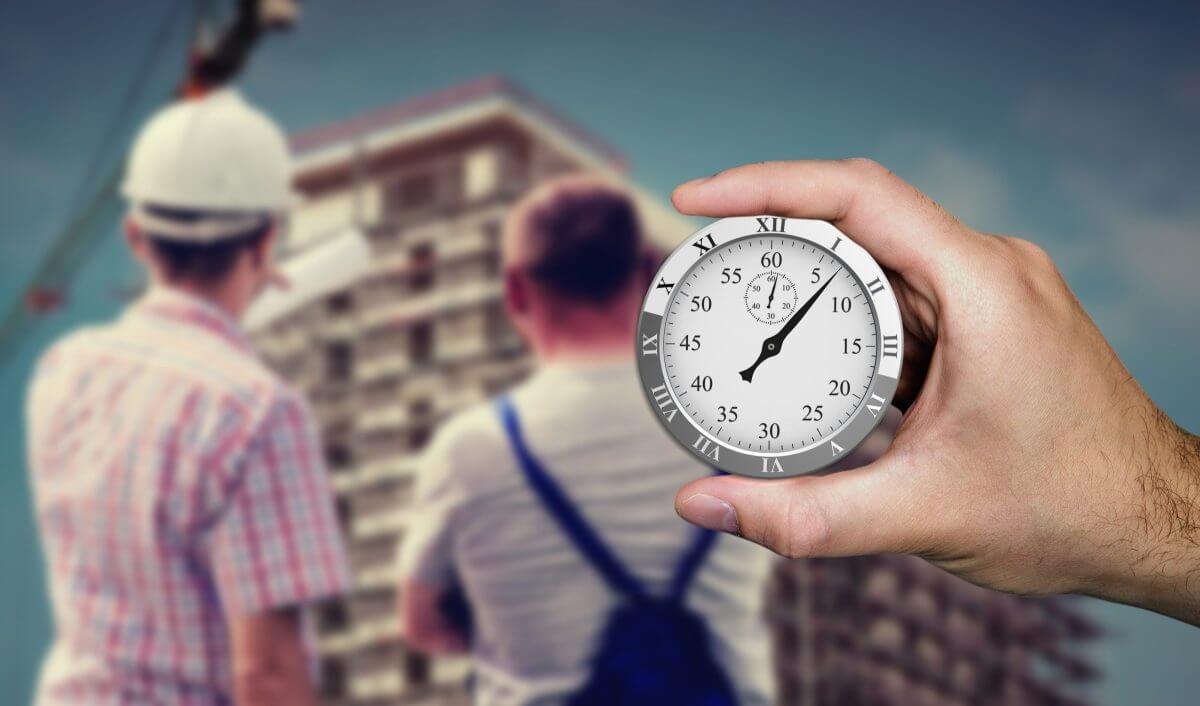 Im Vordergrund eine Stoppuhr, im Hintergrund Bauarbeiter vor einem Rohbau: Symbole für schnellere Bauprozesse.