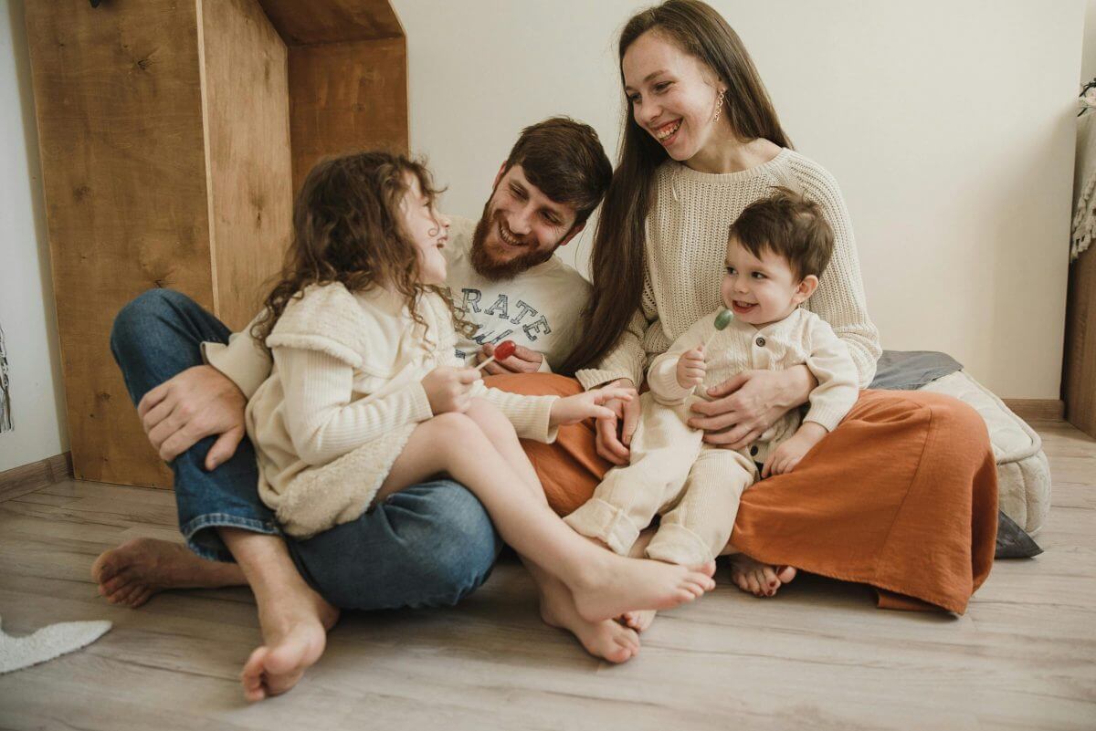Familie mit zwei kleinen Kindern sitzt barfuß auf dem Wohnzimmerboden.