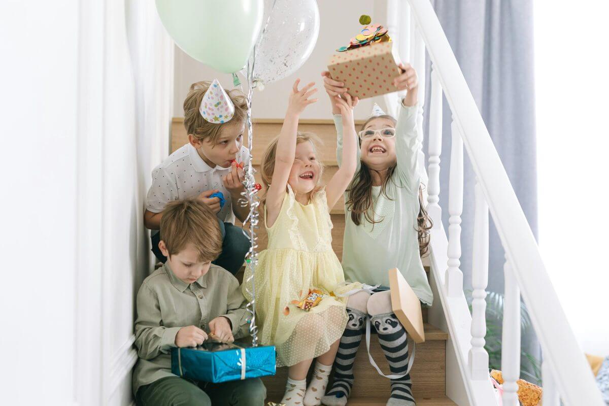 Kinder auf einer Treppe halten Geschenke und Luftballons in der Hand.