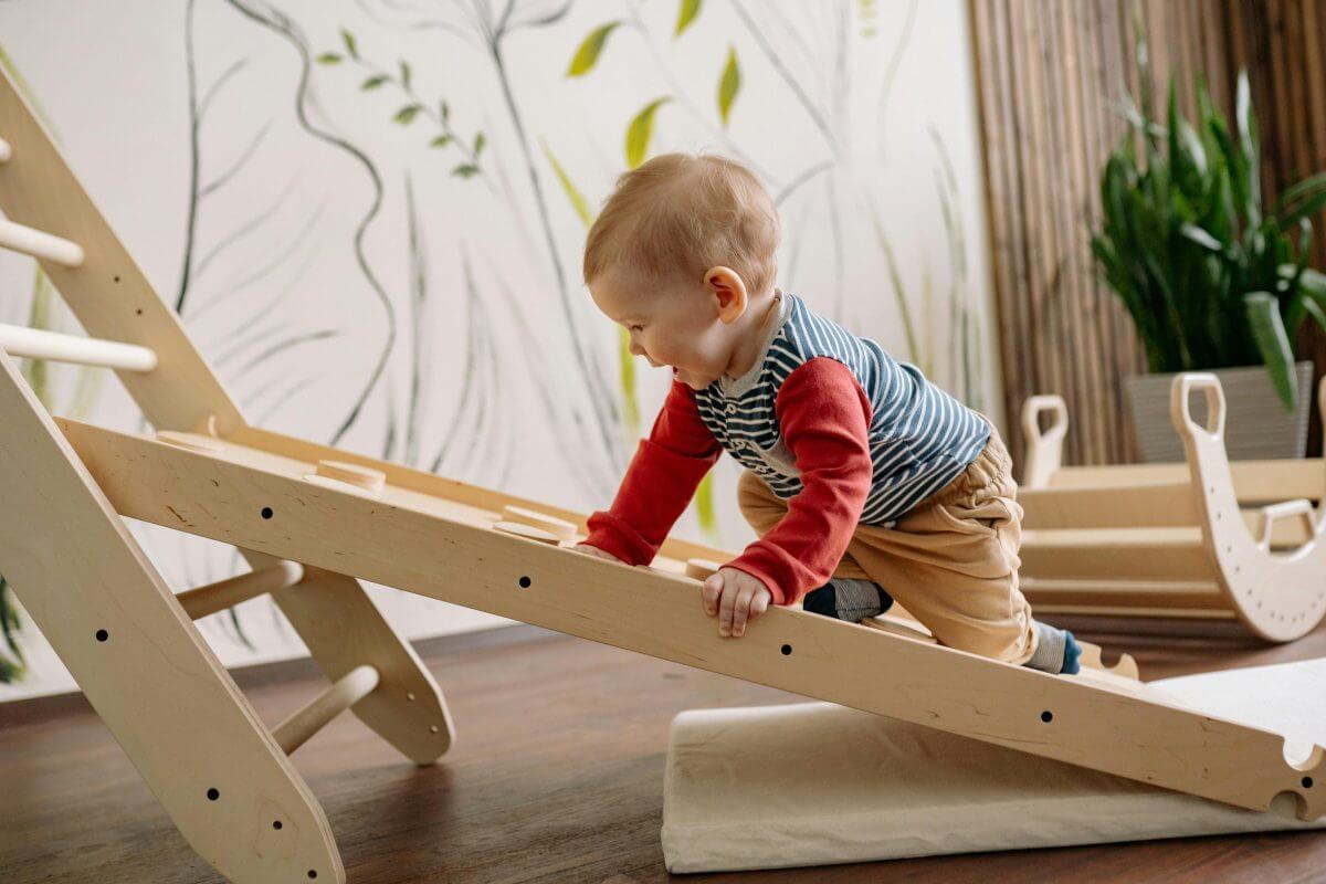Kleinkind klettert eine kleine Holzrampe hinauf.