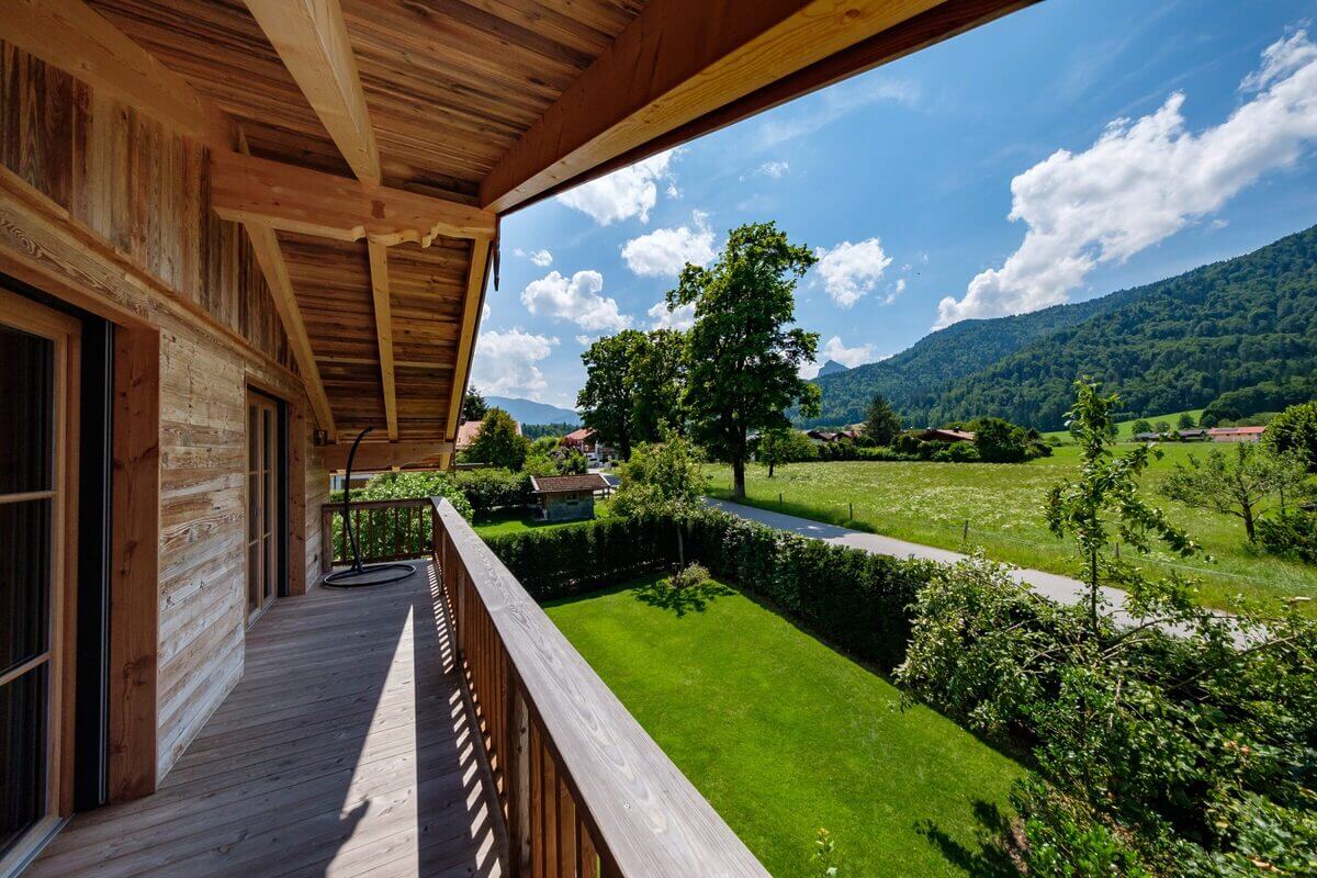 Ein Ferienhaus in der Region Tegernsee mit Holzbalkon, Garten und Ausblick auf Bergwiesen. 