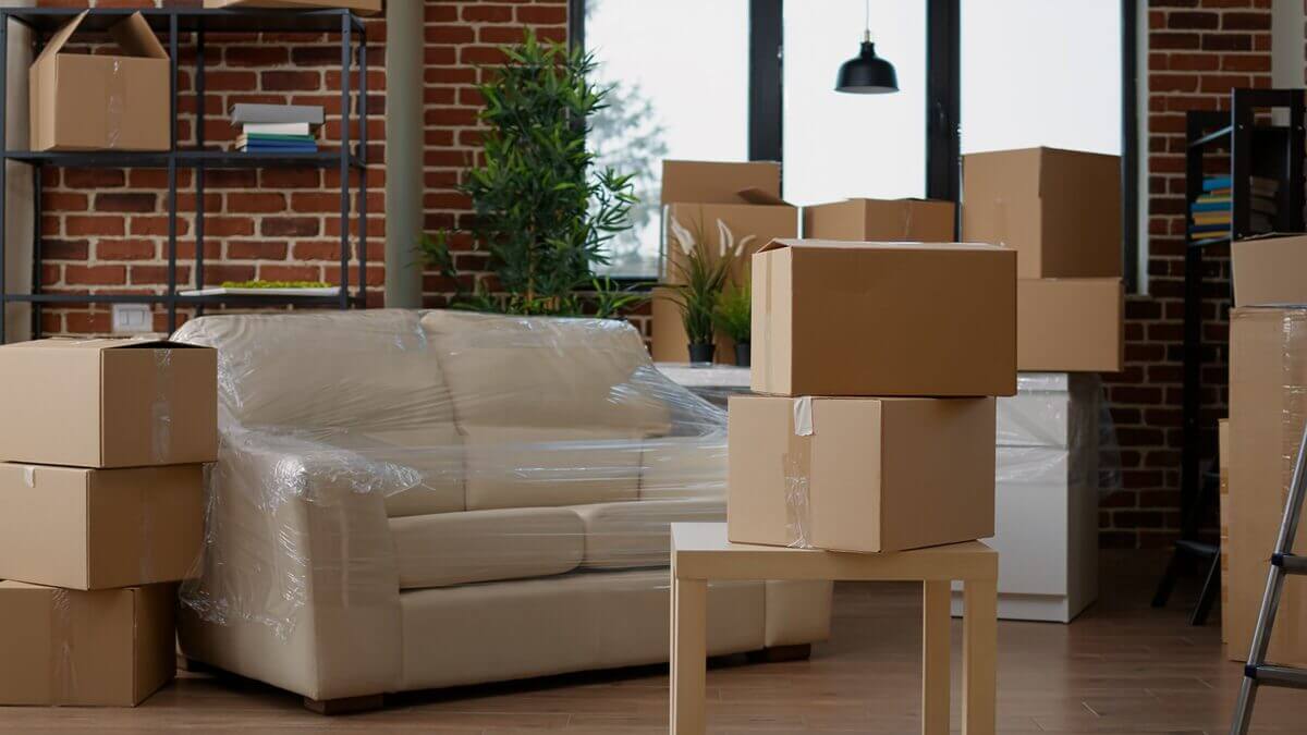 Ein Zimmer mit einem neuen, noch in Plastikfolie verschweißten Sofa und Umzugskartons. 