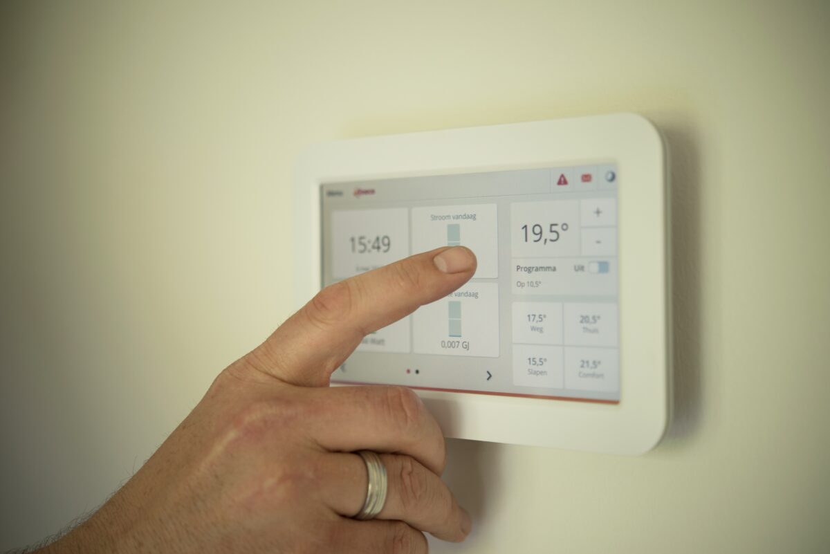 Eine Hand vor einem modernen Smart Meter Gerät an der Wand. 